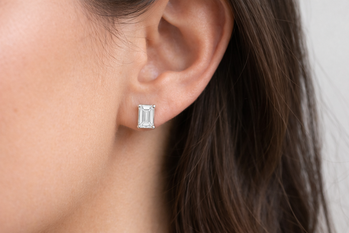 Woman wearing emerald cut diamond stud earrings in white gold by Luxe Alchemy